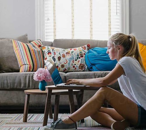Frau sitzt vor Sofa am Laptop