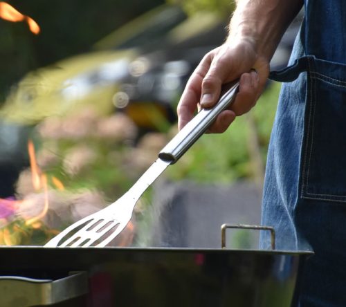 Mensch mit blauer Grillschürze am Grill