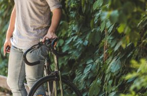 Mann steht neben Fahrrad an einer Hecke